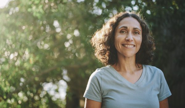 Portrait of a mature woman in sportswear smiling outside in a park on sunny day in summer