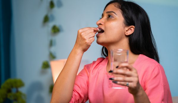 Sick girl taking tablet or medicine pills on bed at home before sleeping at night - concept of medical treatment, insomnia and illness.